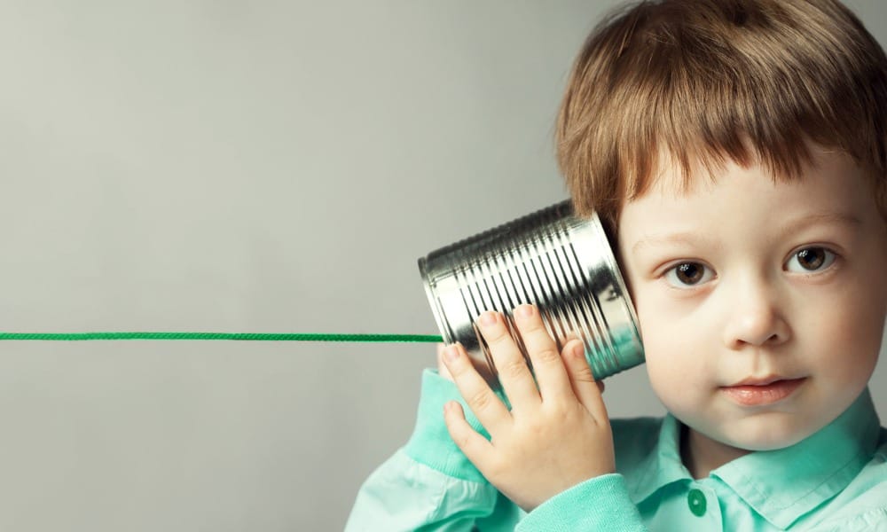 Image of a curious child holding a DIY string can phone to their ear, exploring the concept of communication and connection